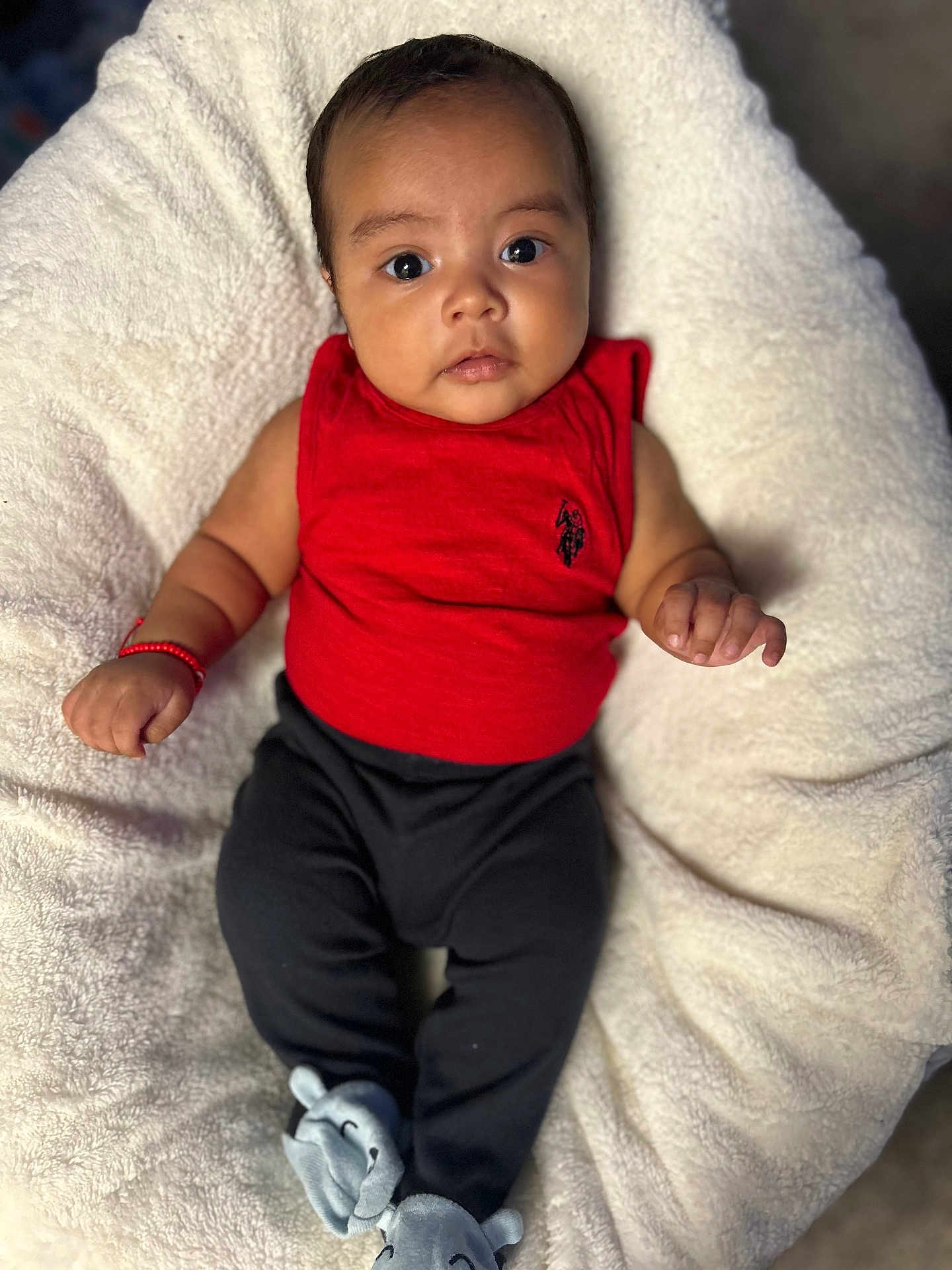 Liam is registered to the contest to win money with this photo: baby, infant, red_shirt, black_pants, elephant_slippers, cushion, white_blanket, face, eyes, hands, feet, sleepwear, portrait, indoor, soft_texture, cute, child, cozy, clothing, relaxing