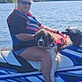 person, dog, water, jet_ski, life_jacket, sunglasses, outdoor, lake, blue_sky, trees, dock, summer, animal, pet, recreation, vehicle, water_sport, sunny, relaxation, vacation