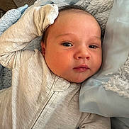 Charlie is registered to the contest to win money with this photo: baby, infant, face, hand, blanket, onesie, clothing, cute, portrait, skin, head, eyes, living_room, fabric, soft_texture, sleepwear, newborn, comfort, resting, closeup