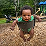 baby, child, swing, playground, green_onesie, wood_chips, trees, stroller, smiling, outdoor, daylight, happy, infant, play, fun, park, person, seat, metal_chains, nature