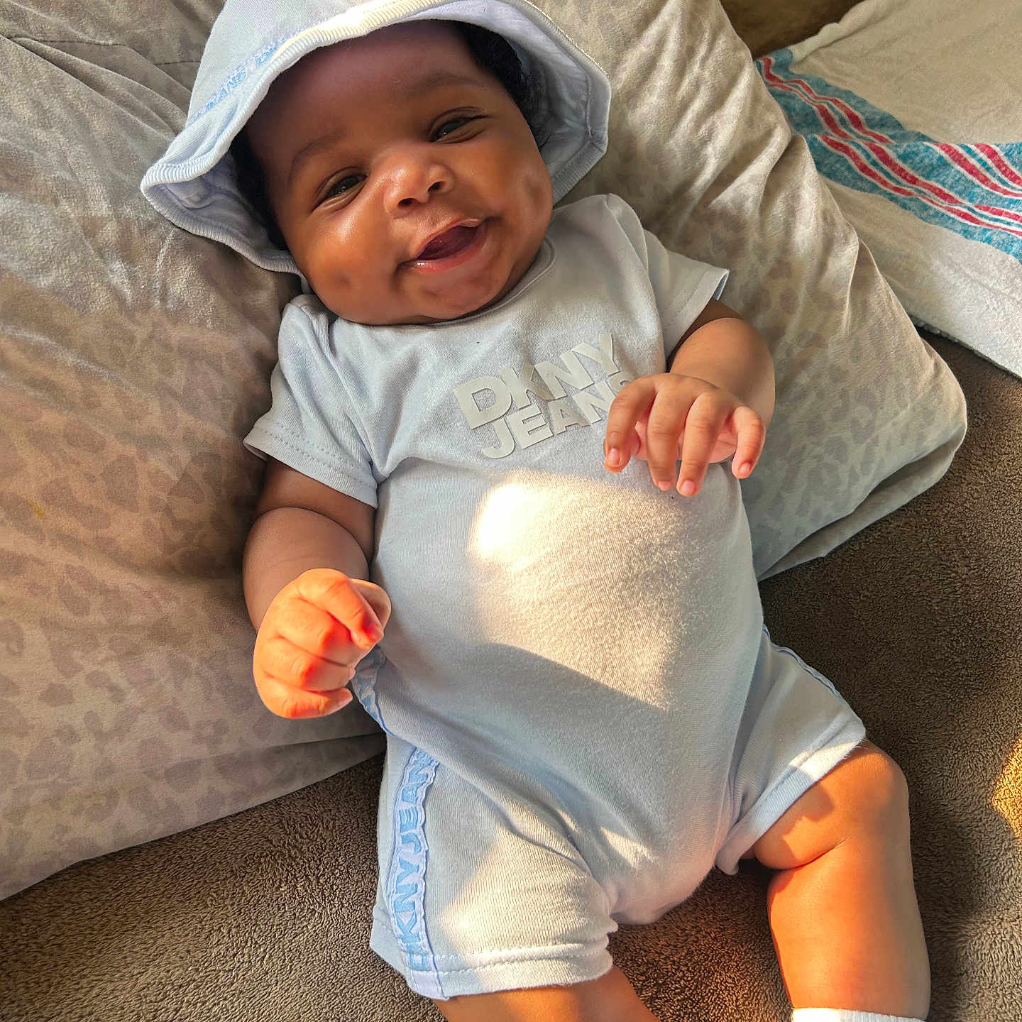 Deomari is registered to the contest to win money with this photo: baby, bed, child, clothing, comfortable, cute, dimples, happy, hat, indoor, infant, light_blue, pillow, portrait, relaxed, smiling, socks, soft, sunlight, toddler