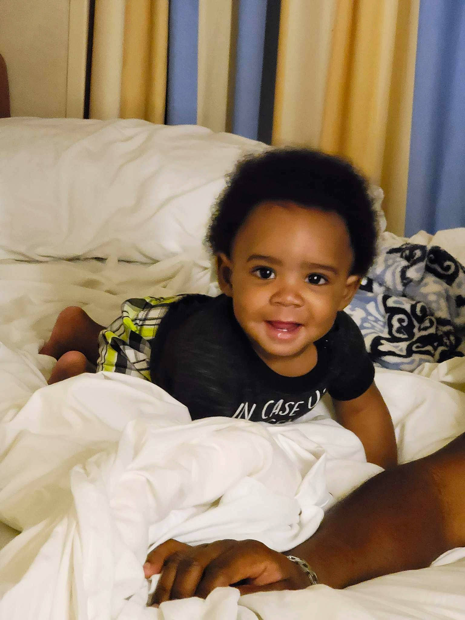 Atreus is registered to the contest to win money with this photo: baby_toddler_clothing, bed, bedding, black_hair, child, comfort, couch, curtain, event, face, fun, happy, linens, person, pillow, room, sitting, smile, t_shirt, textile