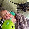baby, infant, child, smiling, happy, portrait, face, indoor, couch, blanket, plush_toy, stuffed_animal, dog, pet, living_room, home, cozy, sitting, pink_clothing, green_toy