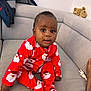 baby, bright_colors, child, clothing, couch, cozy, cute, foot, furniture, home, indoor, infant, looking_at_camera, person, red_pajamas, santa_print, seated, smiling, sofa, teddy_bear