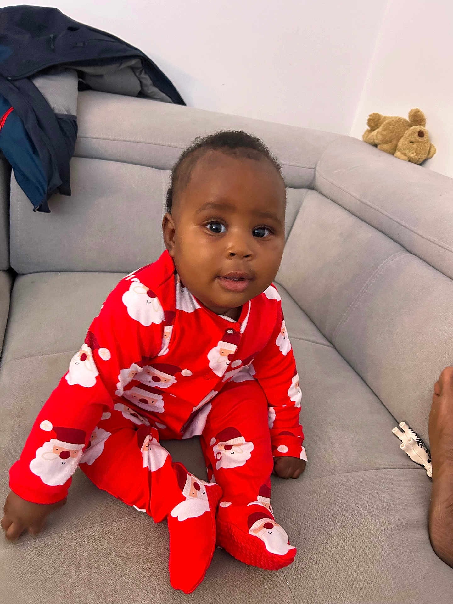 Noura a rejoint le concours — aidez-le/la à gagner de superbes lots ! baby, bright_colors, child, clothing, couch, cozy, cute, foot, furniture, home, indoor, infant, looking_at_camera, person, red_pajamas, santa_print, seated, smiling, sofa, teddy_bear
