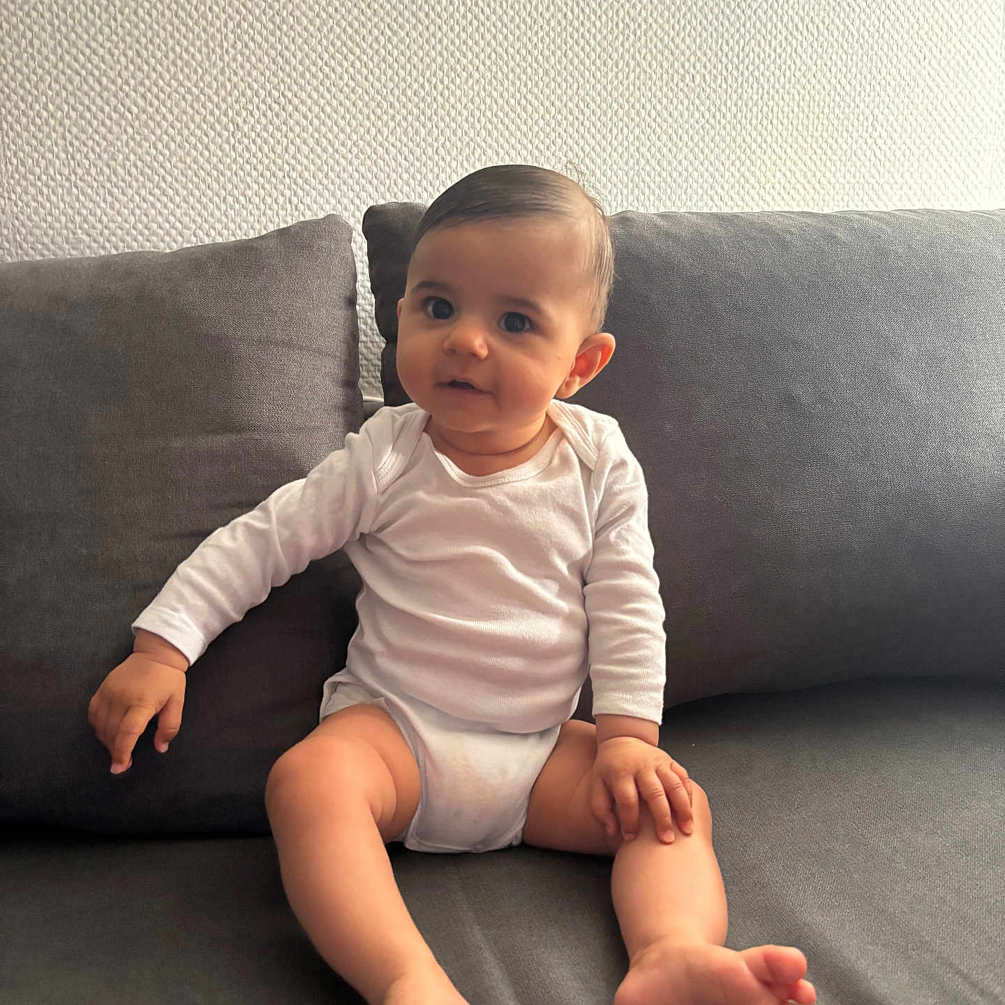 Khewen participe au concours pour gagner de l'argent avec cette photo : baby, barefoot, child, couch, curious, face, foot, furniture, hand, home, indoor, infant, long_sleeve, person, sitting, skin, sofa, texture, wall, white_clothing