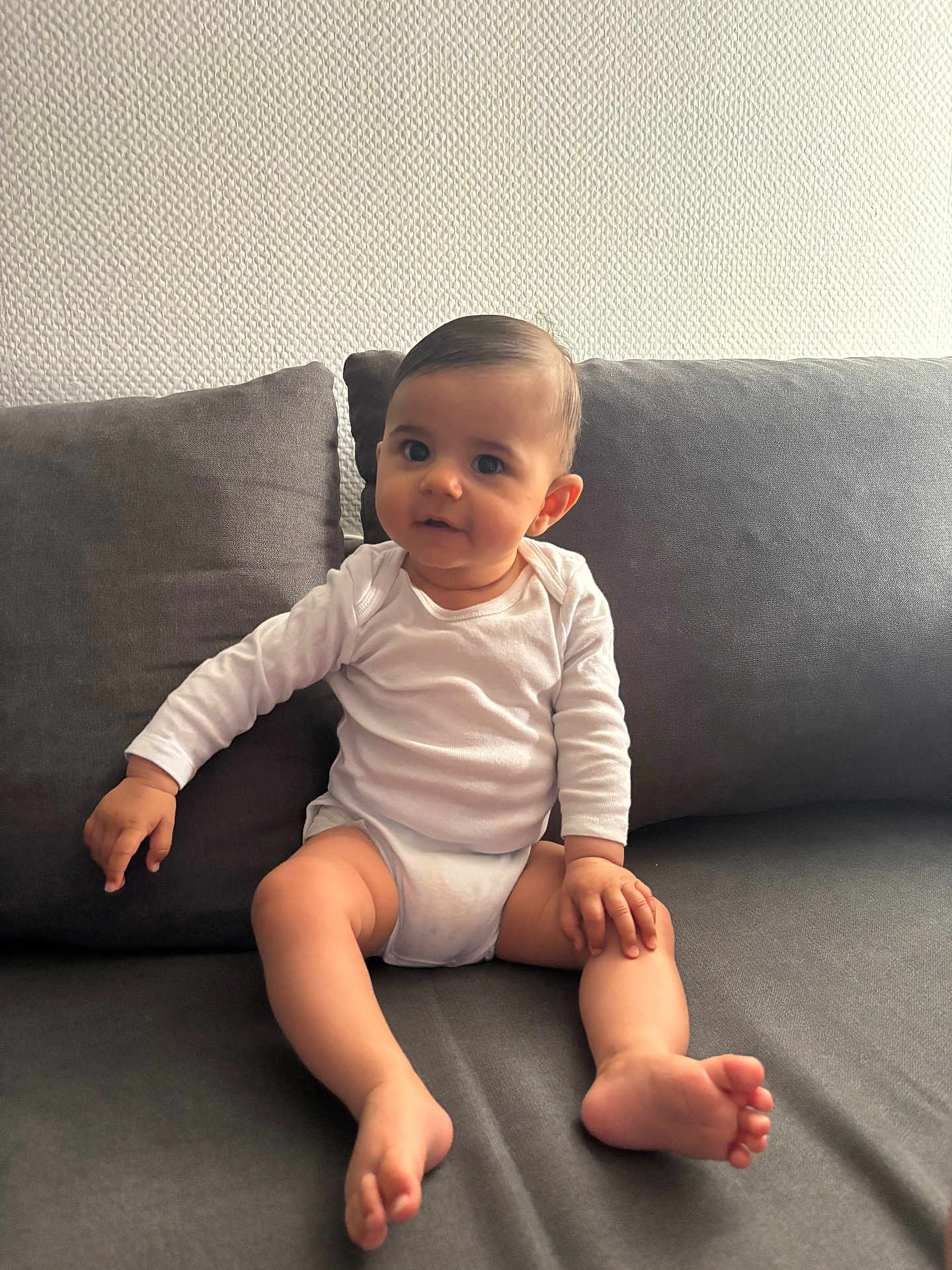 Khewen participe au concours pour gagner de l'argent avec cette photo : baby, barefoot, child, couch, curious, face, foot, furniture, hand, home, indoor, infant, long_sleeve, person, sitting, skin, sofa, texture, wall, white_clothing