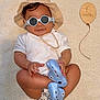 baby, child, sunglasses, hat, blue_crocs, diaper, smile, cute, indoor, milestone, 6_months, wooden_balloon, beige, fashion, portrait, hands, legs, footwear, cool, relaxed
