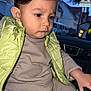 toddler, child, car, steering_wheel, clothing, vest, puffer_jacket, beige_outfit, seat, window, twilight, houses, suburban, hair, face, hand, serious, portrait, indoor, person
