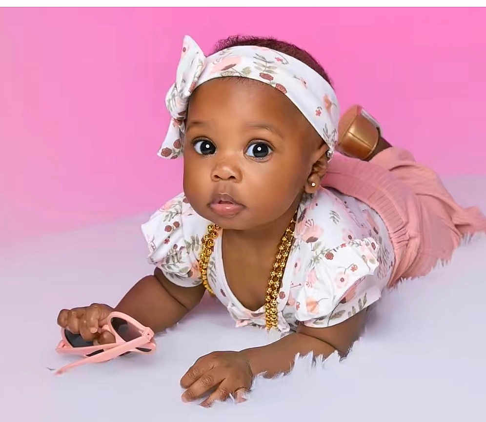 Danielle joined the competition — help win amazing prizes! baby, infant, child, pink_background, headband, floral_outfit, gold_necklace, sunglasses, big_eyes, curious_gaze, studio_photo, crawling_pose, lying_on_stomach, soft_rug, cute, earring, accessory, fashion, portrait, adorable
