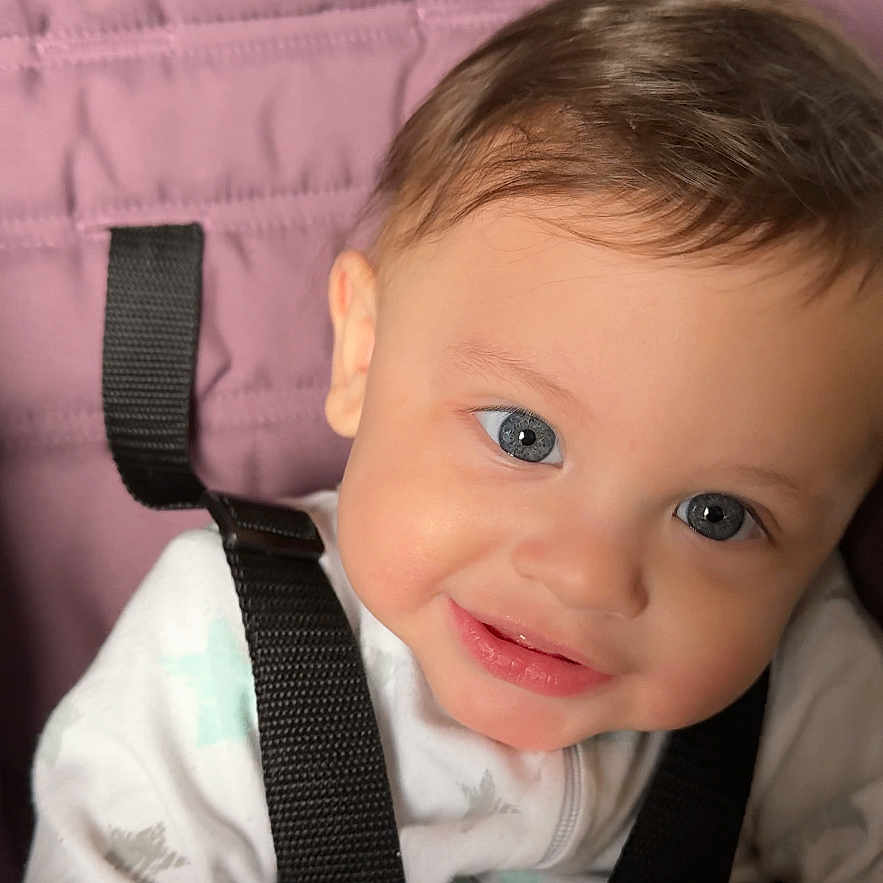 Thomas is registered to the contest to win money with this photo: baby, child, blue_eyes, smile, seatbelt, purple_cushion, clothing, infant, cute, portrait, indoor, straps, happy, young_child, closeup, face, sitting, baby_girl, baby_boy, soft_lighting