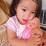 toddler, child, baby_doll, pink_clothing, indoor, hugging, cute, person, face, hand, dark_hair, curious_eyes, soft_skin, casual_wear, toy, close_up, affection, caring, young_child, family