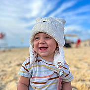 Camille participe au concours pour gagner de l'argent avec cette photo : toddler, child, beach, sand, hat, white_hat, striped_shirt, smiling, happy, baby_teeth, outdoor, sky, clouds, summer, cute, portrait, sitting, playful, sunlight, daytime