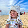toddler, child, beach, sand, hat, white_hat, striped_shirt, smiling, happy, baby_teeth, outdoor, sky, clouds, summer, cute, portrait, sitting, playful, sunlight, daytime