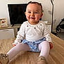Jeanne a rejoint le concours — aidez-le/la à gagner de superbes lots ! baby, child, smiling, sitting, wooden_table, television, framed_photo, floor_lamp, stroller, white_shirt, floral_bloomers, tights, gold_shoes, hair_clip, portrait, indoor, living_room, cute, happy, furniture