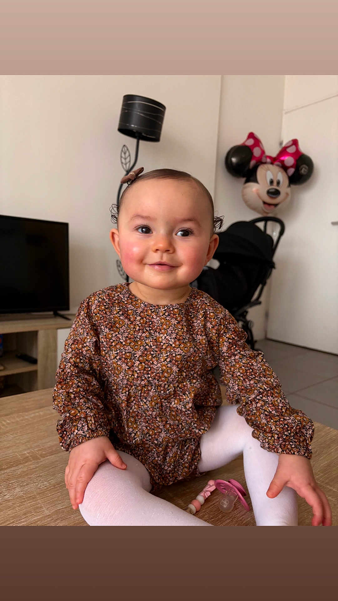 Jeanne a rejoint le concours — aidez-le/la à gagner de superbes lots ! baby, toddler, smiling, indoor, minnie_mouse, balloon, stroller, pacifier, floral_dress, white_tights, wooden_table, living_room, lamp, television, cute, portrait, sitting, toy, happy, child