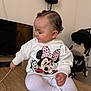 baby, toddler, child, profile, sweatshirt, minnie_mouse, cartoon, bow, hair, table, indoor, stroller, television, lamp, sitting, leggings, white_clothing, cute, hand, wooden_table