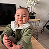 baby, child, collar, cute, furniture, green_coat, hair_buns, hands, indoor, orchid, person, portrait, potted_plant, shoe, sitting, smile, stroller, television, toddler, wooden_table