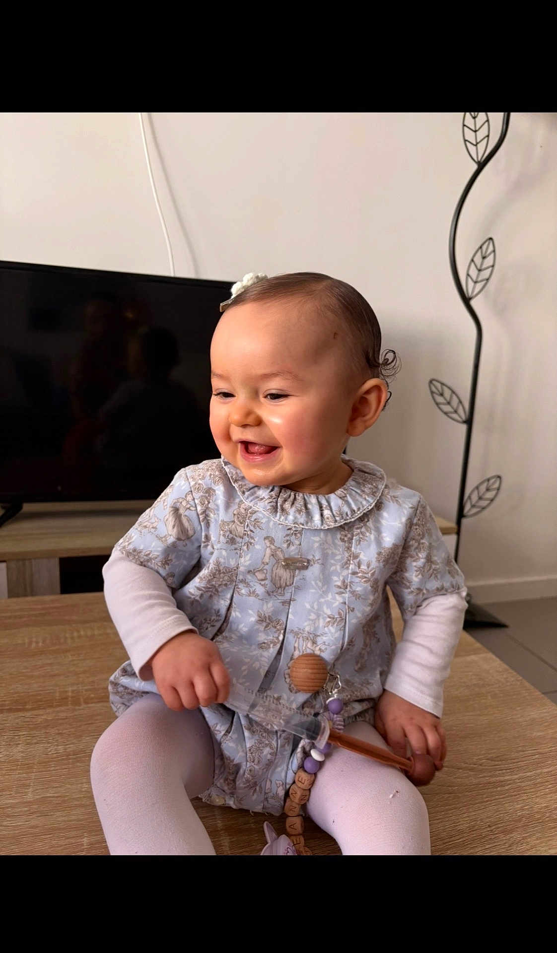 Jeanne participe au concours pour gagner de l'argent avec cette photo : baby, child, smiling, toddler, pacifier, wooden_beads, toy, dress, tights, table, television, reflection, furniture, indoor, hair_clip, sitter, happy, portrait, hands, skin