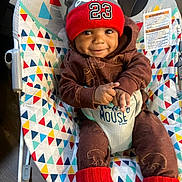 Jayceon joined the competition — help win amazing prizes! baby, child, smiling, hat, red_hat, pom_pom, brown_outfit, baby_rocker, colorful_pattern, indoor, happy, face, person, infant, sitting, cozy, clothing, cute, toy, footwear