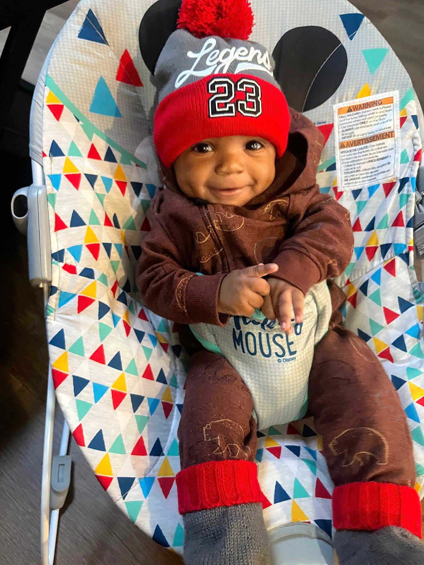 Jayceon joined the competition — help win amazing prizes! baby, child, smiling, hat, red_hat, pom_pom, brown_outfit, baby_rocker, colorful_pattern, indoor, happy, face, person, infant, sitting, cozy, clothing, cute, toy, footwear