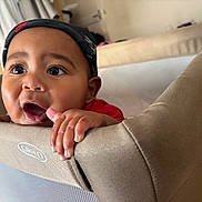 Zane is registered to the contest to win money with this photo: baby, child, infant, face, cap, nike, red_shirt, playpen, fingers, curious, indoors, expression, grip, young, cute, portrait, closeup, skin, headwear, mouth_open