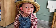 Hector a rejoint le concours — aidez-le/la à gagner de superbes lots ! baby, child, hat, straw_hat, denim_overalls, plaid_shirt, toy_car, pink_ball, floor, wood_floor, indoor, smile, cute, playtime, sitting, person, young_child, cheeks, blue_eyes, casual_clothing