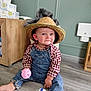 baby, child, hat, straw_hat, denim_overalls, plaid_shirt, toy_car, pink_ball, floor, wood_floor, indoor, smile, cute, playtime, sitting, person, young_child, cheeks, blue_eyes, casual_clothing