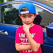 Bentley joined the competition — help win amazing prizes! child, boy, portrait, outdoors, blue_car, baseball_cap, backwards_cap, pink_shirt, thinking_pose, hand_on_chin, crossed_arms, short_hair, smiling, face, person, vehicle, car_door, car_window, reflection, residential_background