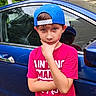 Bentley is registered to the contest to win money with this photo: child, boy, portrait, outdoor, car, blue_car, baseball_cap, backward_cap, pink_shirt, t_shirt, standing, pose, thoughtful, face, eyes, brown_hair, vehicle, driveway, house, daylight