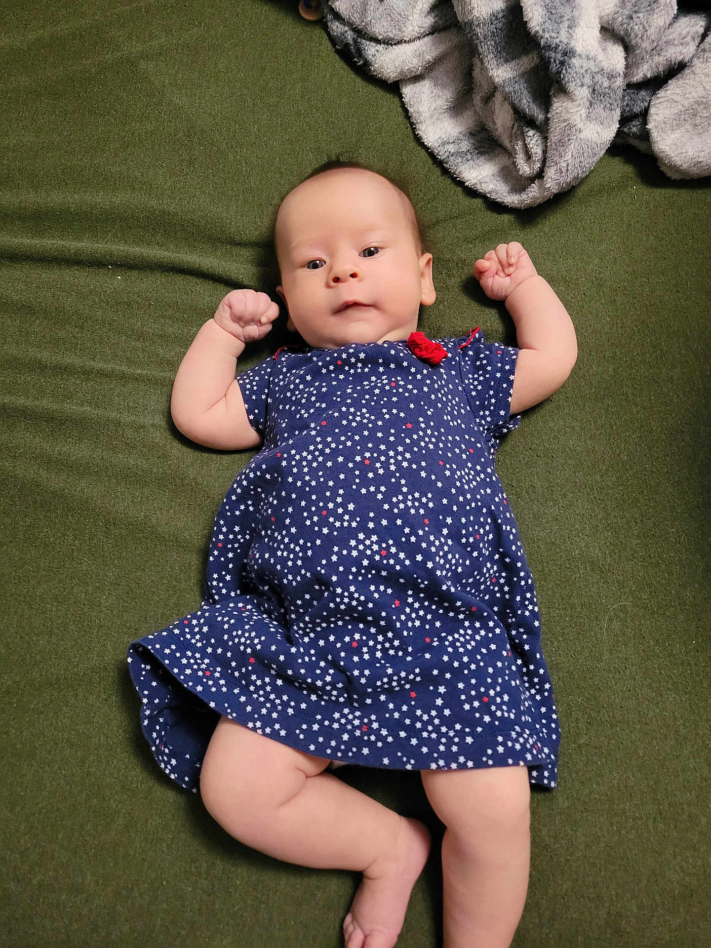 Amara is registered to the contest to win money with this photo: baby, infant, child, dress, blue_dress, stars_pattern, blanket, green_blanket, gray_blanket, lying_down, raised_arms, curious_expression, indoor, soft_texture, cute, small_fists, person, infant_clothing, portrait, newborn