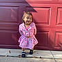 child, girl, pink_clothing, checkered_pattern, smiling, hair_accessories, shoes, sidewalk, autumn_leaves, outdoor, garage_door, concrete, fall, cute, portrait, standing, casual, daylight, happy, young