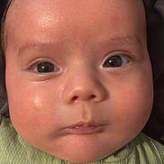 Patricio is registered to the contest to win money with this photo: baby, close_up, face, chubby_cheeks, green_clothing, button, infant, skin, eyes, expression, head, portrait, child, young, cute, indoors, person, human, small, adorable