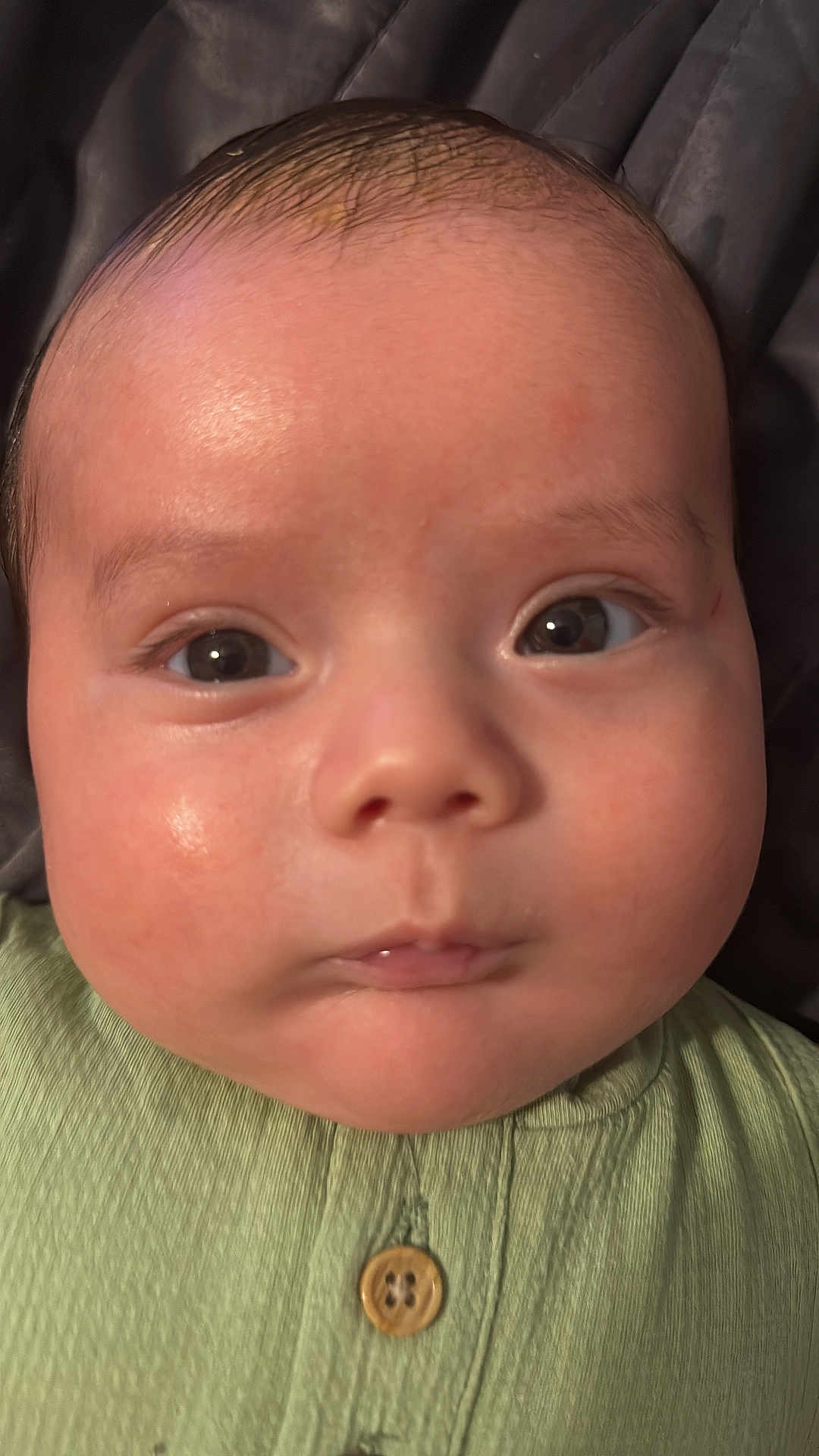 Patricio is registered to the contest to win money with this photo: baby, close_up, face, chubby_cheeks, green_clothing, button, infant, skin, eyes, expression, head, portrait, child, young, cute, indoors, person, human, small, adorable