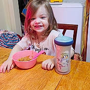 Braelyn joined the competition — help win amazing prizes! toddler, child, smiling, table, noodles, pink_bowl, spoon, sippy_cup, kitchen, washing_machine, toy, wooden_table, person, indoor, happy, meal, clothing, furniture, hair, face