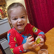 Cailyn joined the competition — help win amazing prizes! child, toddler, smiling, pajamas, toy, slime, table, kitchen, chair, curtain, red_curtain, wooden_furniture, happy, indoor, play, hands, face, person, home, cute