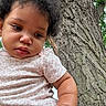 Zayla is registered to the contest to win money with this photo: baby, child, portrait, outdoor, tree, tree_trunk, nature, infant, curly_hair, pink_clothing, patterned_shirt, close_up, face, eyes, serious_expression, sitting, daylight, park, wood, photography
