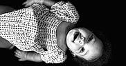 Zayla is registered to the contest to win money with this photo: baby, child, portrait, black_and_white, lying_down, wide_eyes, curly_hair, patterned_clothing, gingham, floral, dress, infant, face, eyes, indoor, studio, photography, monochrome, adorable, close_up