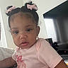 Zayla is registered to the contest to win money with this photo: baby, child, infant, portrait, face, pink_bows, hair_bows, curious, indoor, home, living_room, television, pink_shirt, sitting, close_up, candid, dark_hair, looking_at_camera, furniture, daylight