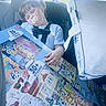 car_interior, car_seat, child, clothing, crayons, cute, daylight, indoor, pacifier, person, pillow, portrait, relaxed, seatbelt, sleeping, stickers, toddler, toy_box, window, young_child