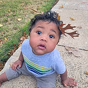 Oden is registered to the contest to win money with this photo: toddler, child, curly_hair, autumn_leaves, outdoor, grass, sidewalk, gray_shirt, colorful_stripes, sitting, cute, wide_eyes, nature, fall, leaf_crown, concrete, casual_clothing, curious_expression, young_child, daylight