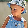 child, toddler, boy, hat, bucket_hat, dinosaur_print, overalls, blue_clothing, summer, outdoor, portrait, cute, face, skin, eyes, expression, sunlight, bokeh, casual, young