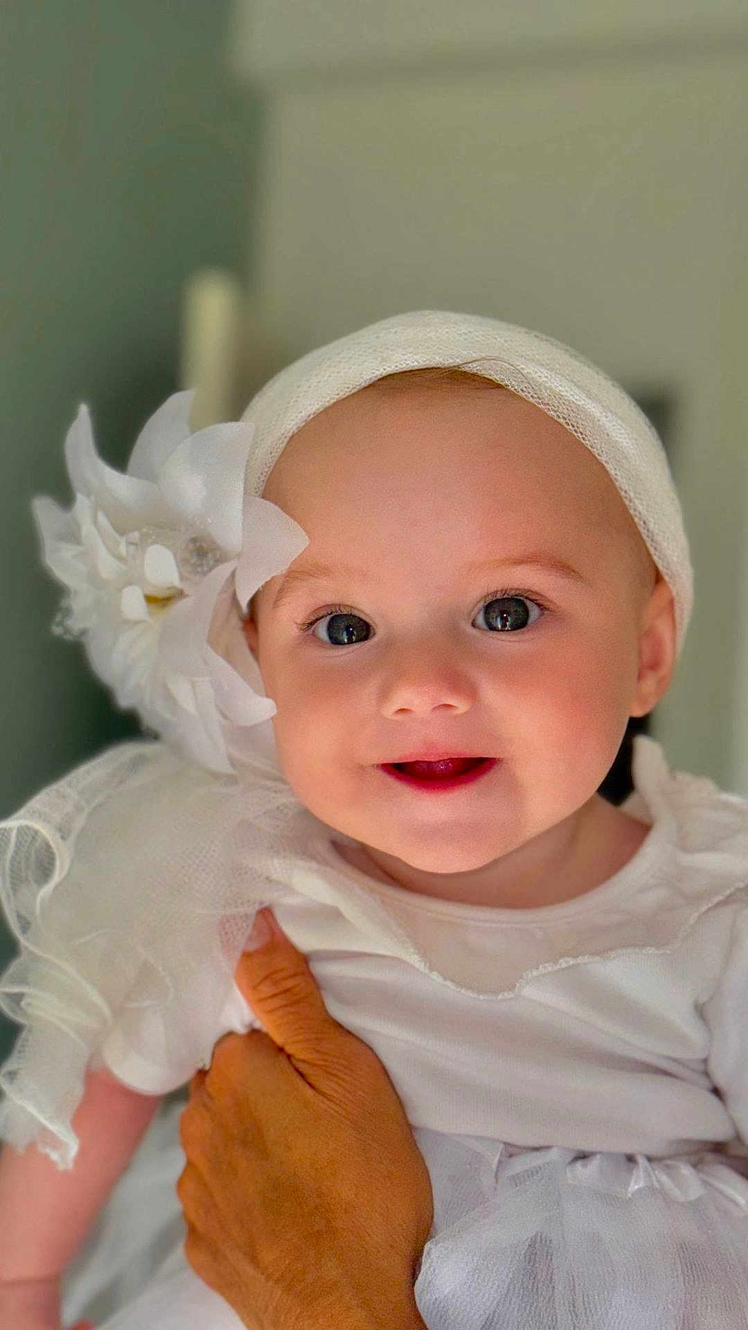 Sérena participe au concours pour gagner de l'argent avec cette photo : baby, child, smile, face, headband, flower, white_clothing, hand, adult_hand, portrait, closeup, cute, infant, happy, soft_light, indoors, tulle, dress, skin, eyes