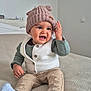 Isodaurío a rejoint le concours — aidez-le/la à gagner de superbes lots ! baby, child, hat, pink_hat, vest, white_vest, long_sleeve_shirt, green_shirt, pants, beige_pants, socks, gray_socks, bed, bedspread, indoor, person, smiling, cute, playful, seated