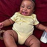 baby, infant, smiling, yellow_onesie, red_couch, milk_bottle, teething_toy, happy, child, sitting, cute, chubby_arms, chubby_legs, indoors, portrait, playful, young_child, furniture, cozy, person