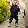 toddler, child, nike, tracksuit, sneakers, green_shoes, sidewalk, car, reflection, bush, outdoor, concrete, building_wall, window_shutter, standing, young_child, person, casual_clothing, daylight, walking