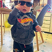 Brenn-Arthur is registered to the contest to win money with this photo: boy, cabinet, casual_clothing, chair, child, cute, expression, floor, hoodie, hot_wheels, indoor, kitchen, person, playful, standing, sunglasses, table, toddler, toy, young_child