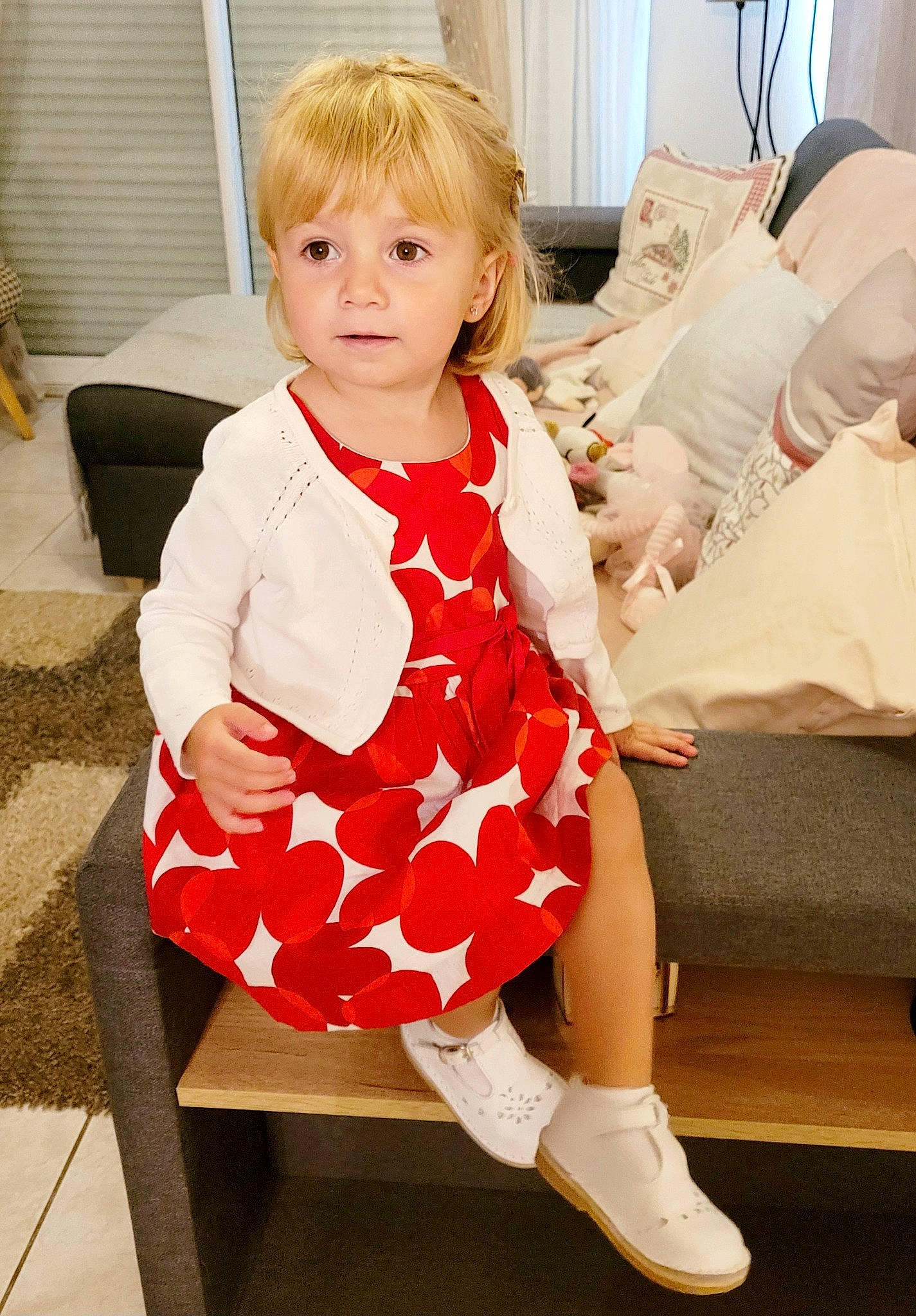 Inés participe au concours pour gagner de l'argent avec cette photo : baby_toddler_clothing, blond, child, comfort, couch, dress, event, face, formal_wear, hair, happy, human_leg, joint, knee, leg, pattern, person, sleeve, sock, thigh