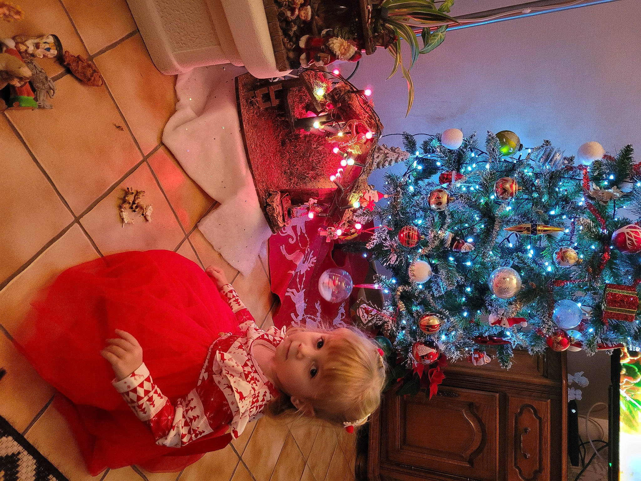 Inés participe au concours pour gagner de l'argent avec cette photo : baby, christmas, christmas_decoration, christmas_eve, christmas_ornament, christmas_tree, event, flooring, fun, holiday, holiday_ornament, ornament, person, plant, red, room, snapshot, toddler, tree, white