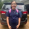 child, girl, smiling, backpack, cross_necklace, rain, wet_hair, car, suv, vehicle, outdoor, driveway, tshirt, shorts, person, portrait, daytime, casual_clothing, standing, happy